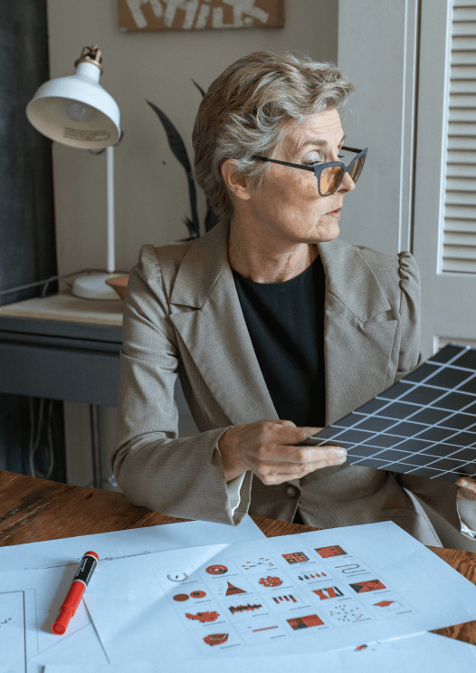 une femme avec une veste kaki et un tshortnoir qui tient un classeur à carreaux noir devant son bureau, services digitaux