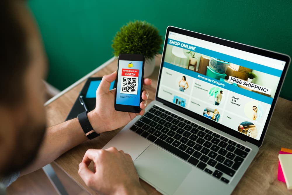 un homme flouté vu de dos qui tient un téléphone devant son ordinateur, créer site e-commerce