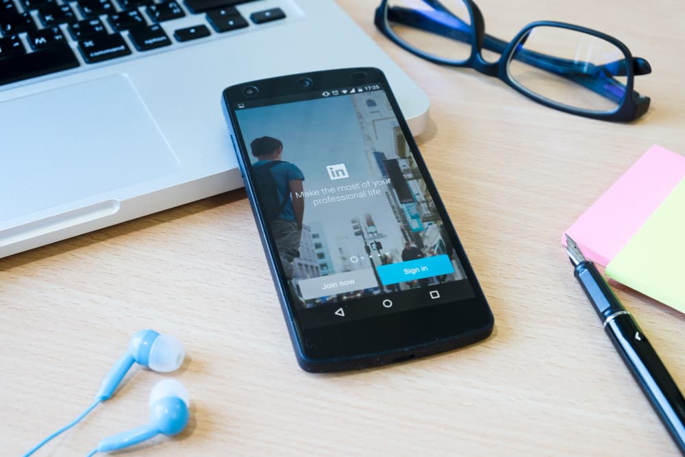 la page Linkedin sur un écran de smartphone, posé sur un ordinateur portable, avec un style et des écouteurs à côté, stratégie LinkedIn PME