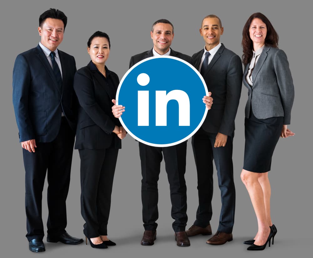 un groupe de 3 hommes et deux femmes cadres en costumes qui tiennent un logo Linkedin, stratégie LinkedIn PME